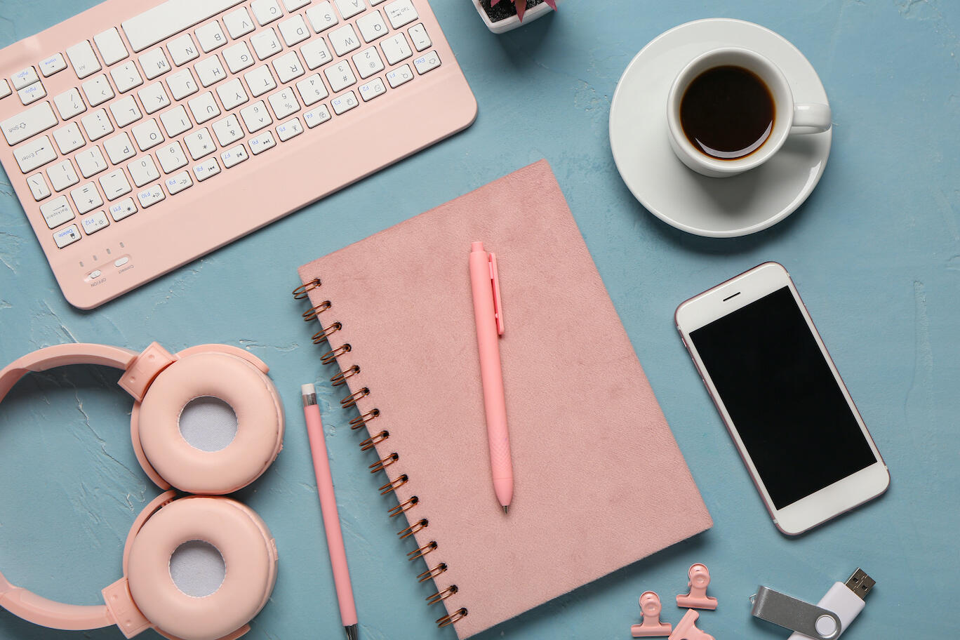 Creative desk flatlay with coral keyboard, headphones, smartphone, and notebook, representing tech support, website updates, and design services for small businesses.