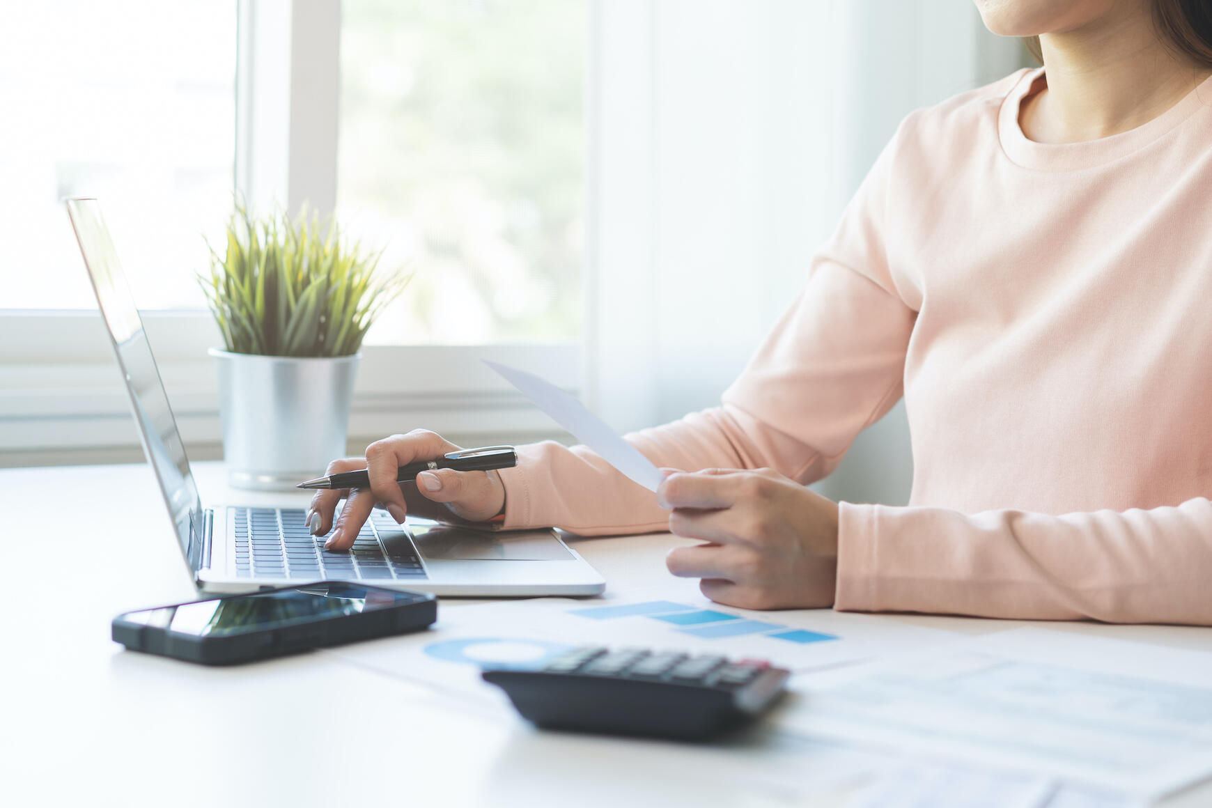 Woman working at laptop with papers and calculator, illustrating business and operations support for small businesses.