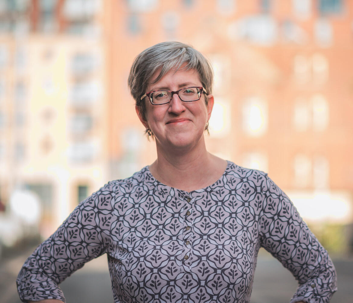 Mia Walker | Virtual Assistant & Business Support Mia Walker, Virtual Assistant and coach, smiling in a power pose with blurred city backdrop.